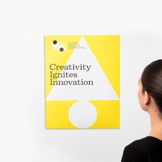 A woman standing in front of a yellow and white wall decal printed with Creativity Ignites Innovation.