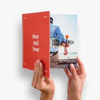 Two hands holding open a spiral bound booklet printed with a red cover and deer and beer in white text.