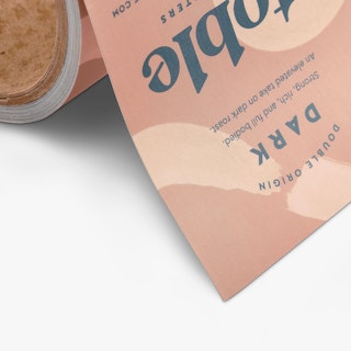 The bottom corner of a square roll label printed with Double Origin Dark and coffee bean details.
