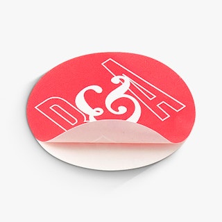 A round sticker seal peeling off its backing and printed with a bright pink and white design.