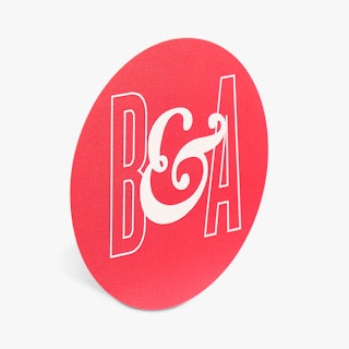 A custom sticker seal printed with a round design and B & A in white on a bright pink background.