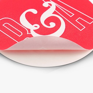 A custom sticker seal peeling off its backing and printed with a bright pink and white design.