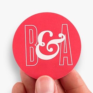 A hand holding a sticker seal custom printed with a bright pink and white design.
