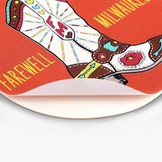 A custom sticker peeling off its backing and printed with an orange cowboy boot design.