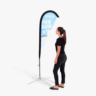 A woman wearing a black shirt and jeans standing next to a teardrop feather flag in white, blue and black.