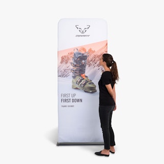 A woman in black standing next to a three-foot tension fabric display printed with a ski boot.