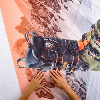 Two hands laying on top of a tension fabric display graphic printed with a snowy mountain and ski boot.