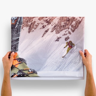 Two hands holding a folded fabric graphic printed with a person skiing down a mountain and a ski boot.