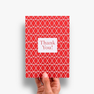 A hand holding a thank you card printed with a red and white geometric design on the front.