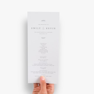 A hand holding a custom wedding program with Emily & Kevin and the names in their wedding party.