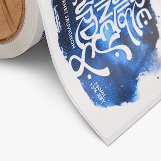 The bottom corner of a wine label on a roll and printed with a blue, black and white design.
