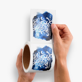 Two hands holding a roll of wine labels printed with a black, white and blue design.