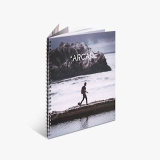 A wire bound booklet printed with a black coil and a cover with Arcade in white text and a person walking on a path between water.