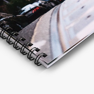 The bottom corner of a wire coil booklet with black coils in sets of two through square drill holes.