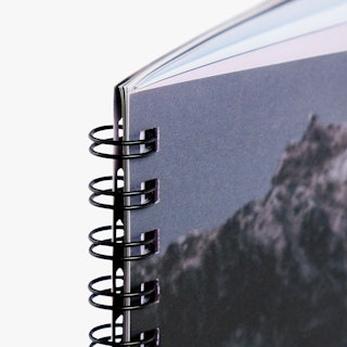 The top left corner of a booklet bound with black wire coils in sets of two through square drill holes.