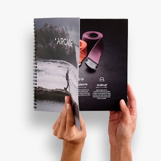 Two hands holding open a wire coil booklet with Arcade printed on the cover and an image of straps inside.